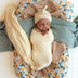 Newborn baby wrapped in lemon swaddle with matching headband, lying on a citrus-patterned blanket.